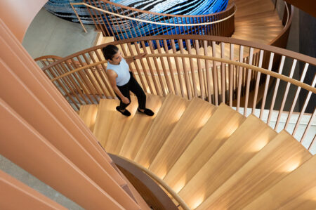 A person ascending a spiral staircase in a office building.