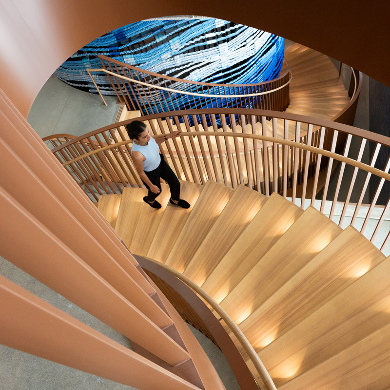 A person ascending a spiral staircase in a office building.