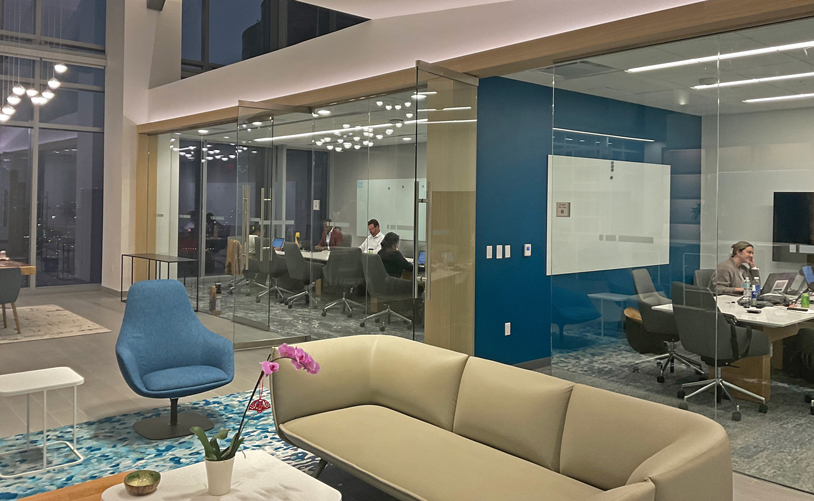 A contemporary office featuring a spacious glass wall and stylish blue chairs.