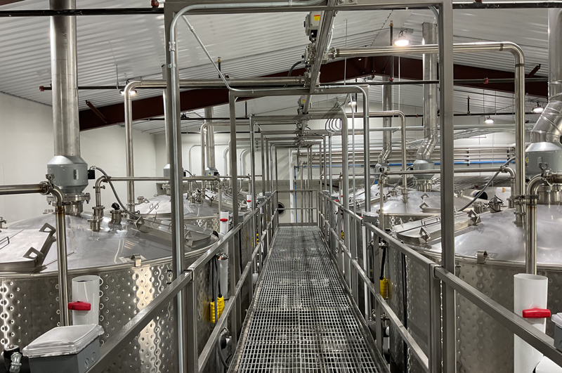 A line of tanks in a distillery, used for fermenting and storing. The tanks are shiny and cylindrical in shape.