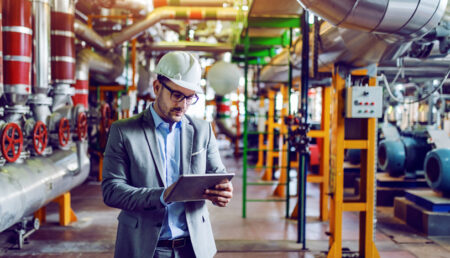 A construction professional in a suit and hard hat is utilizing a tablet device for work purposes.