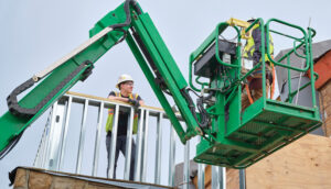 Two construction workers wearing PPE, with one inside a crane.