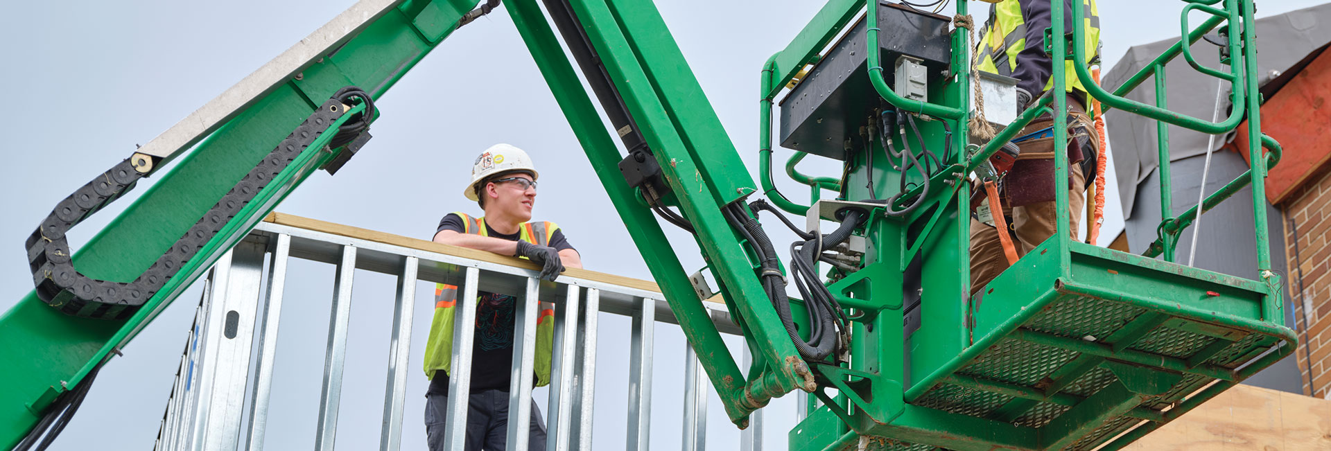 Two construction workers wearing PPE, with one inside a crane.