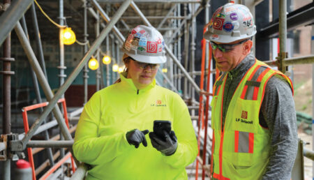 Two construction workers wearing full PPE looking at a phone