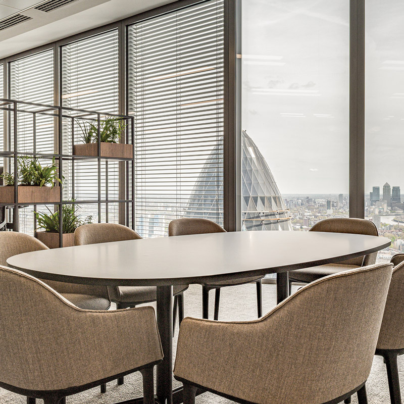 A table and chairs near floor to ceiling windows that overlook the city of London.