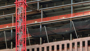 A red crane positioned next to a building under construction.