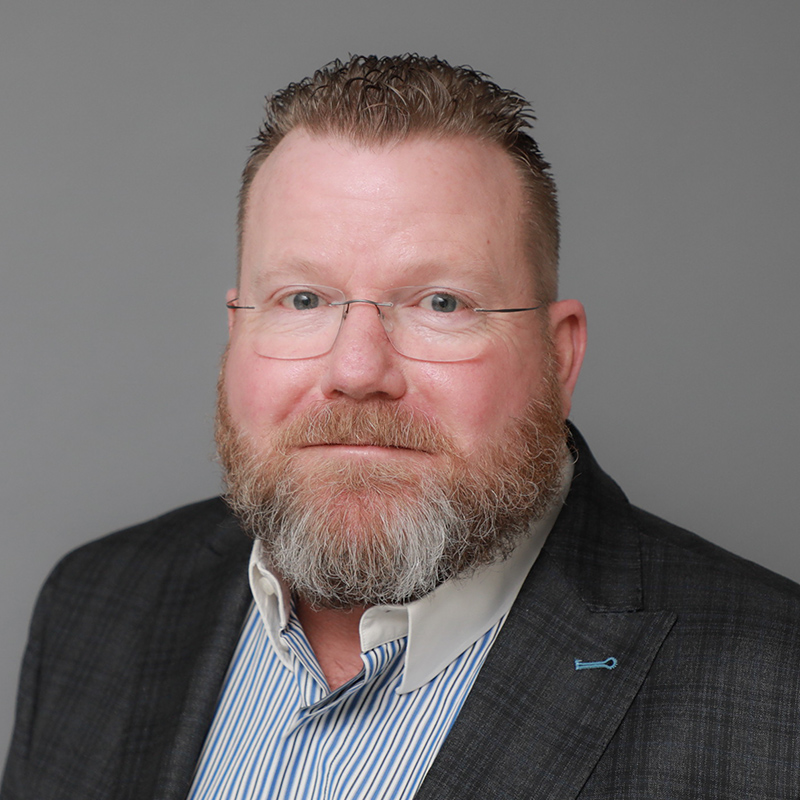 Michael Walsh headshot with grey background blue shirt and suit jacket