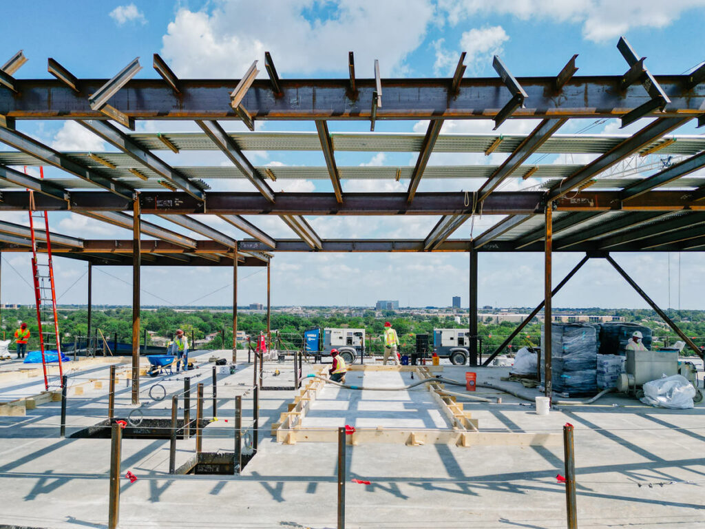 Wide-angle view of a multi-story building under construction, showing an exposed steel frame with horizontal and vertical beams forming the structure.