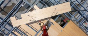 Trusting in Timber: What Commercial Tenants Should Consider in Hybrid CLT Buildings A crane lifts a large mass timber panel into place within a steel building frame as workers guide the installation from below, viewed from directly overhead.