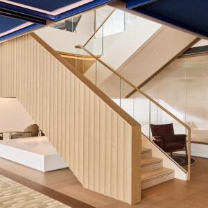 A Step-By-Step Guide to CLT Staircases Modern office staircase with light wood paneling, glass railings, integrated lighting, and seating areas beneath a dark blue ceiling.