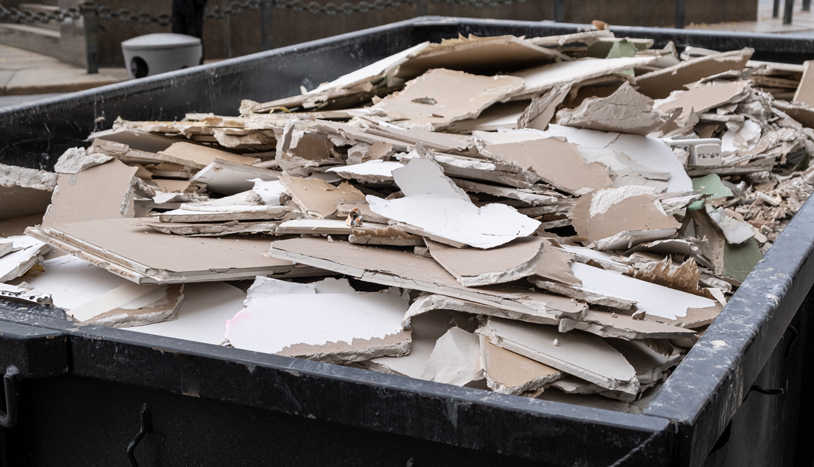 Construction dumpster filled with broken drywall and other demolition debris.