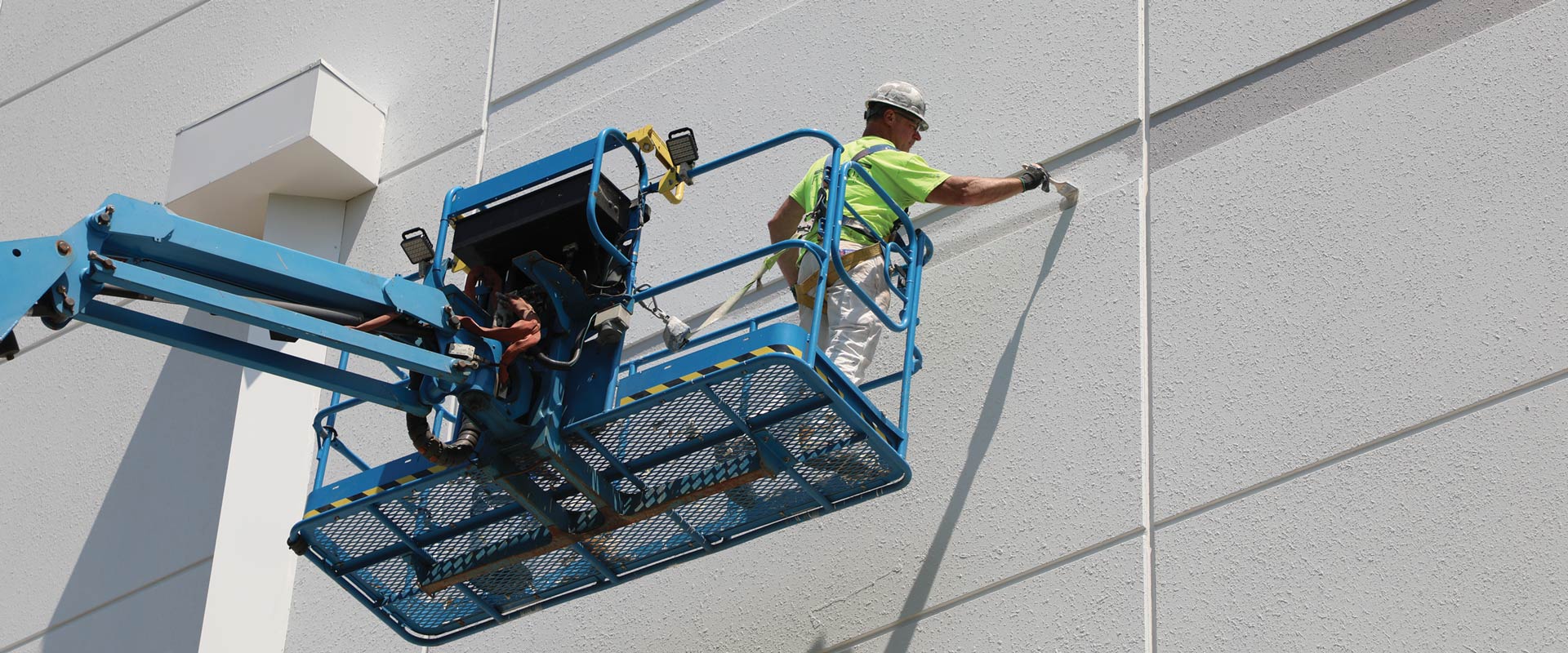 Worker on an elevated blue lift applying material to the exterior wall of a building.