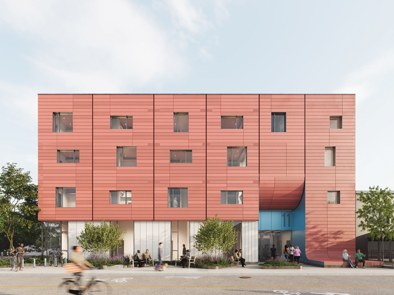 Front view of a red-paneled multistory building with a blue recessed entrance marked 11, sidewalk plantings, pedestrians, outdoor seating, bicycles, and a cyclist in the foreground.