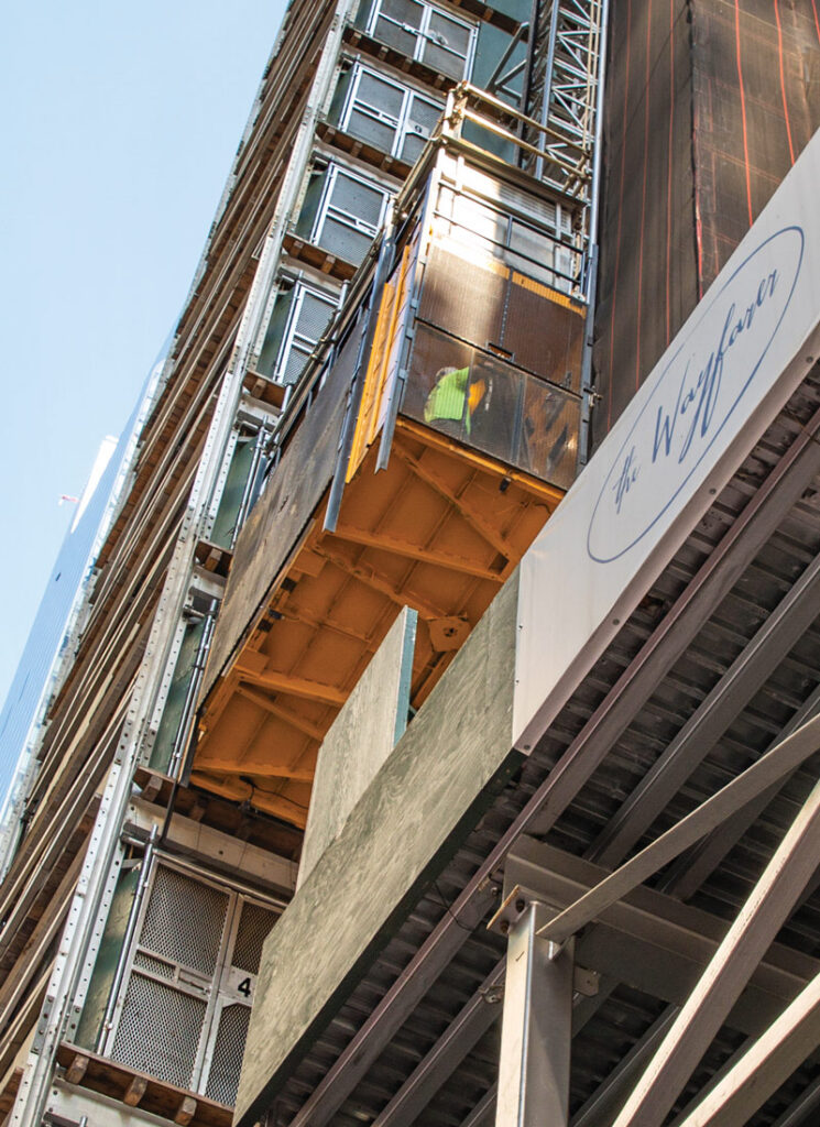 Worker in a temporary construction hoist beside a building facade.