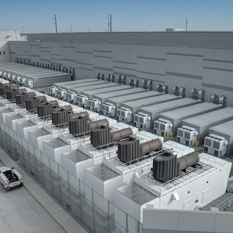 Exterior of a large industrial building with rows of rooftop mechanical equipment, cooling units, ductwork, and service platforms.