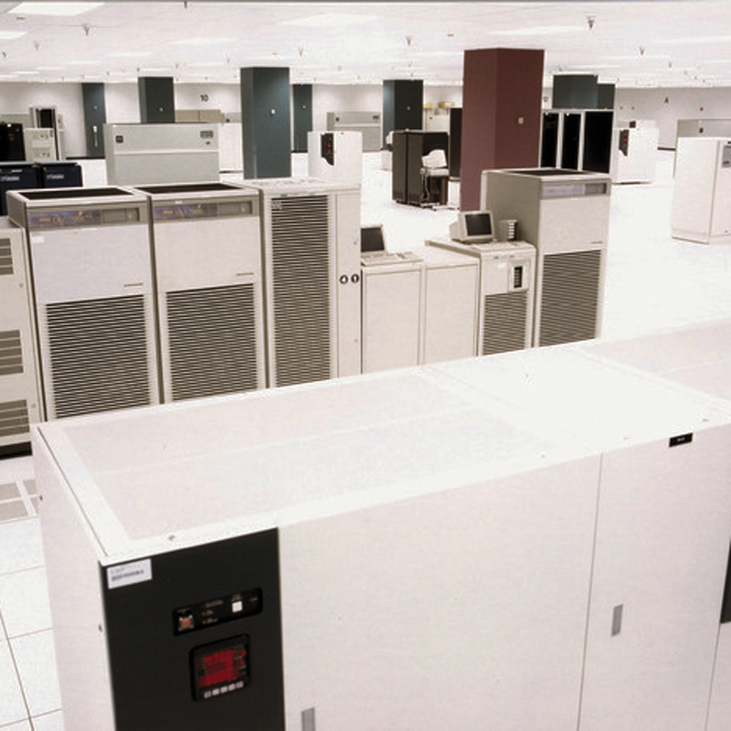 Interior of a brightly lit equipment room with rows of large white and gray electrical cabinets and control units.